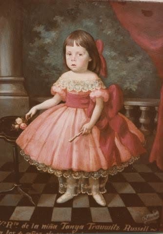 Niña con vestido rosa de volantes de pie sobre un piso de baldosas en damero, ante una cortina y una balaustrada